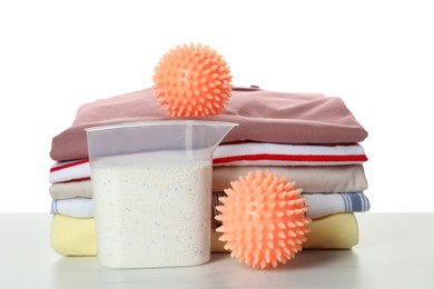 Orange dryer balls, detergent and stacked clean clothes on marble table against white background