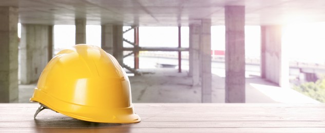 Image of Hard hat on white wooden surface at construction site with unfinished building, banner design. Space for text 