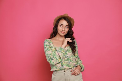 Beautiful young woman with straw hat on pink background
