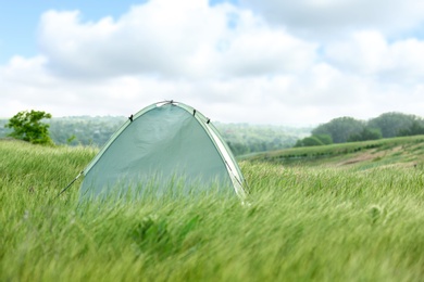 Photo of Modern camping tent in green field on sunny day. Space for text