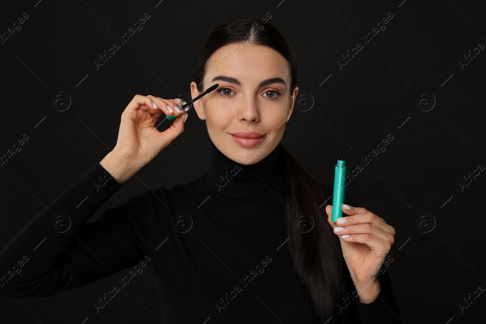 Photo of Beautiful young woman applying mascara on black background