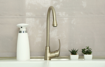 Photo of Modern automatic soap dispenser near sink indoors