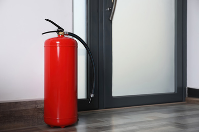 Photo of Fire extinguisher near door indoors. Space for text