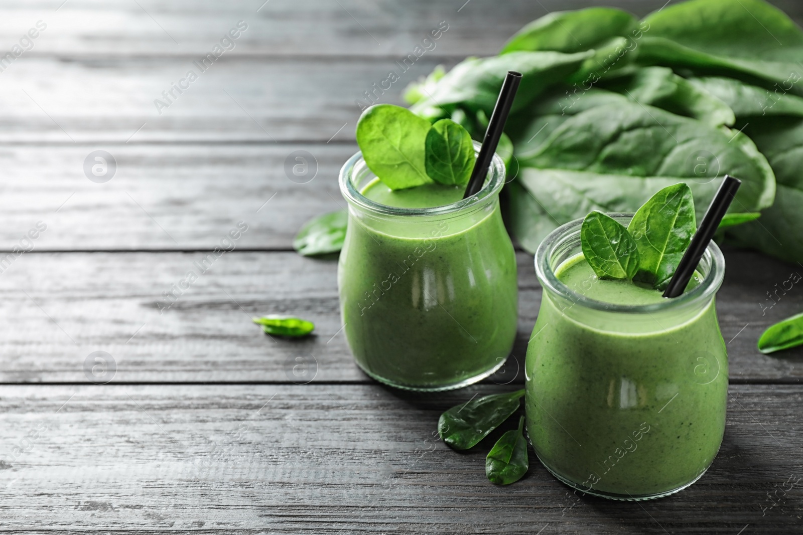 Photo of Jars of healthy green smoothie with fresh spinach on grey wooden table. Space for text