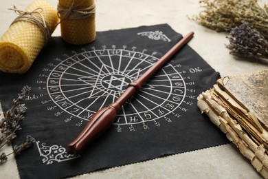 Photo of Magic wand, divination cloth, old book and wax candles on light table, closeup