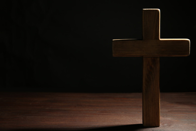 Photo of Christian cross on wooden table against black background, space for text. Religion concept