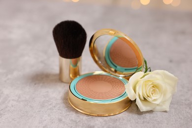 Photo of Bronzer, brush and rose flower on grey textured table, closeup