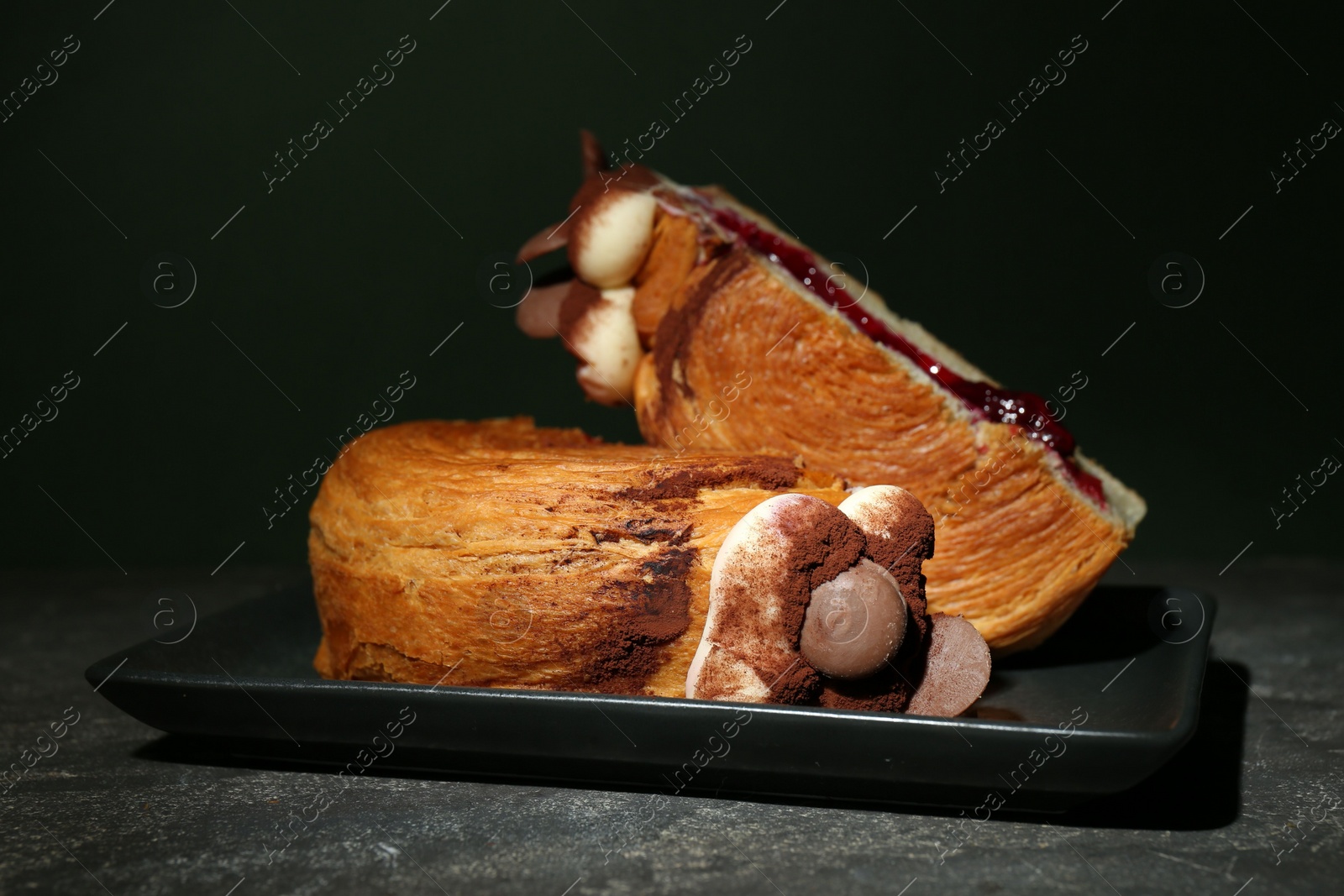 Photo of Round croissant with jam, cream and chocolate chips on grey table. Tasty puff pastry