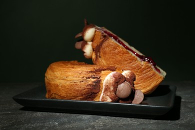 Photo of Round croissant with jam, cream and chocolate chips on grey table. Tasty puff pastry