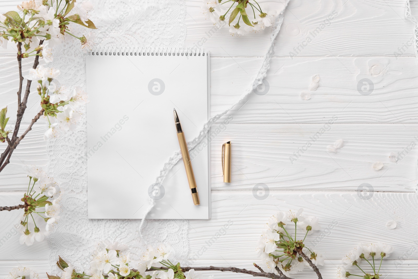 Photo of Guest list. Notebook, pen, spring tree branches with beautiful blossoms and lace ribbons on white wooden background, flat lay. Space for text