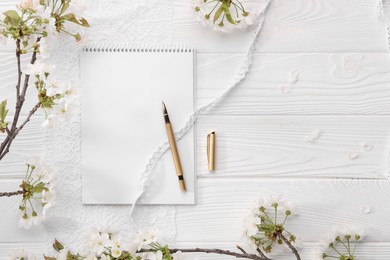 Guest list. Notebook, pen, spring tree branches with beautiful blossoms and lace ribbons on white wooden background, flat lay. Space for text