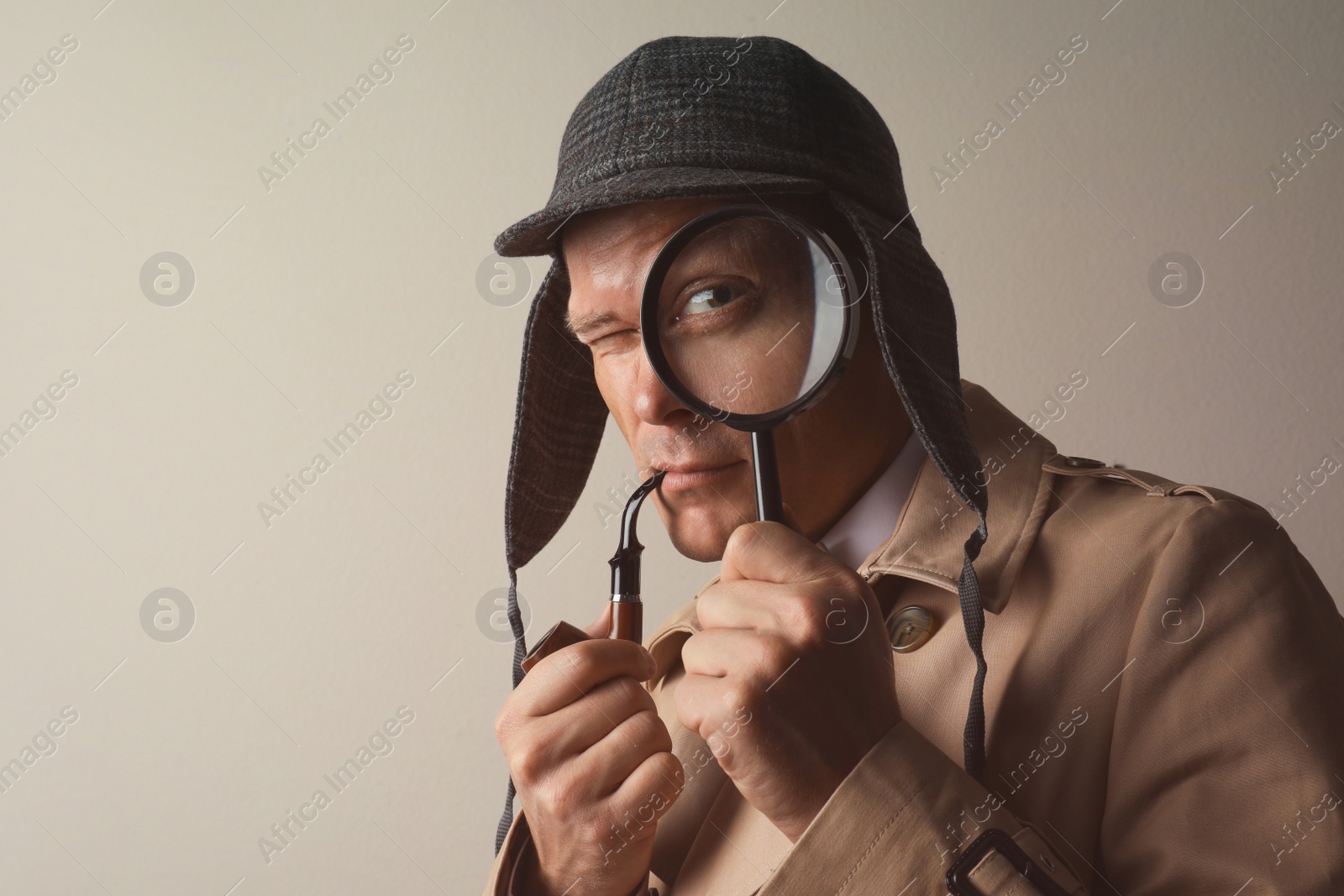 Photo of Male detective with smoking pipe looking through magnifying glass on beige background. Space for text