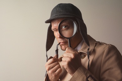 Photo of Male detective with smoking pipe looking through magnifying glass on beige background. Space for text