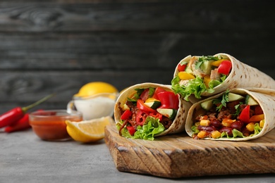 Board with delicious meat tortilla wraps on light table against black background