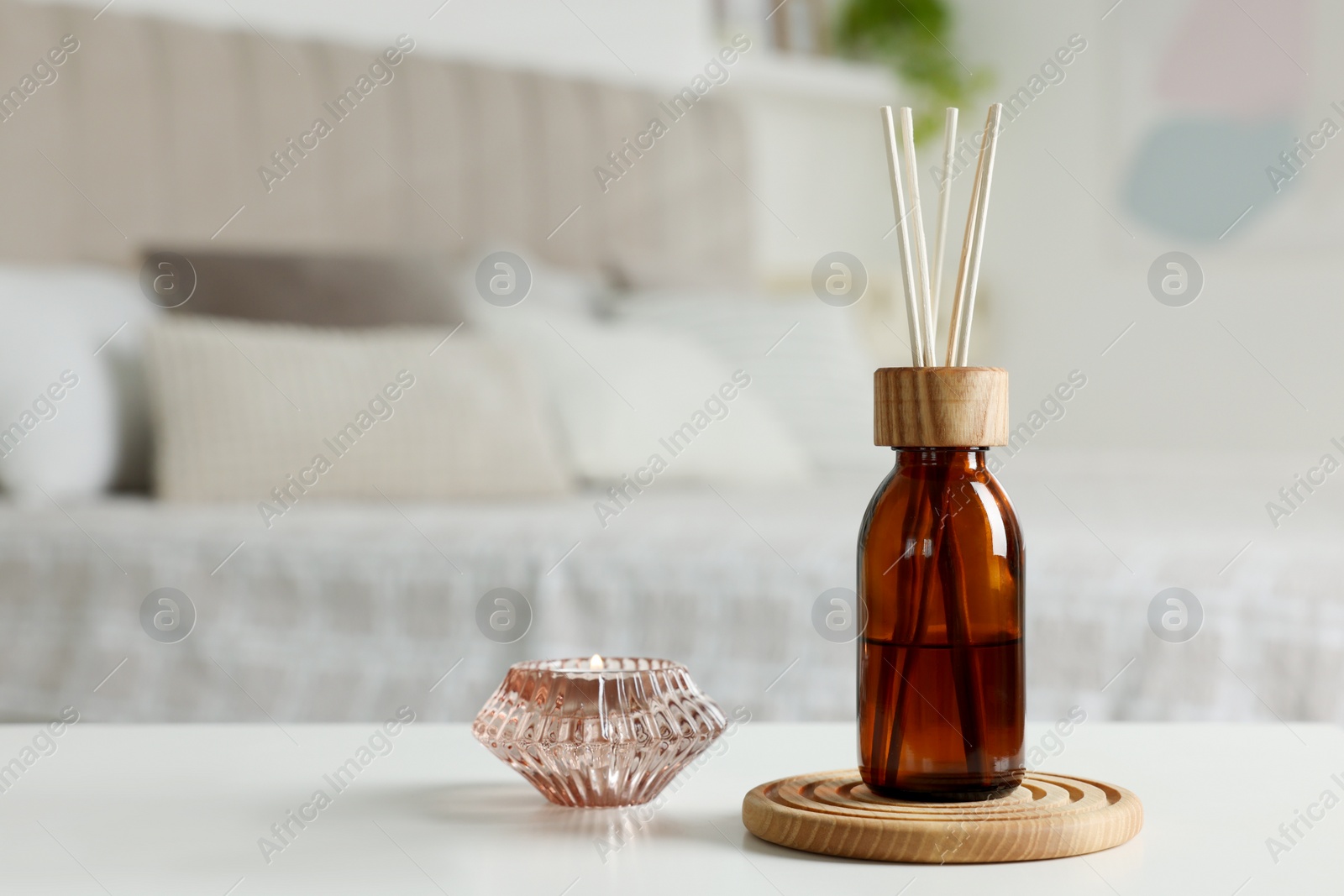 Photo of Aromatic reed air freshener and candle on white table in bedroom. Space for text