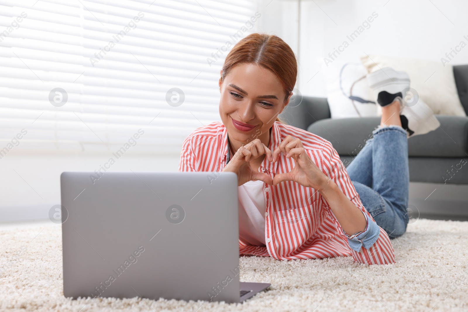 Photo of Woman making heart with hands during video chat via laptop at home. Long-distance relationship