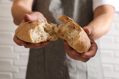 Photo of Man breaking loaf of fresh bread near white brick wall, closeup