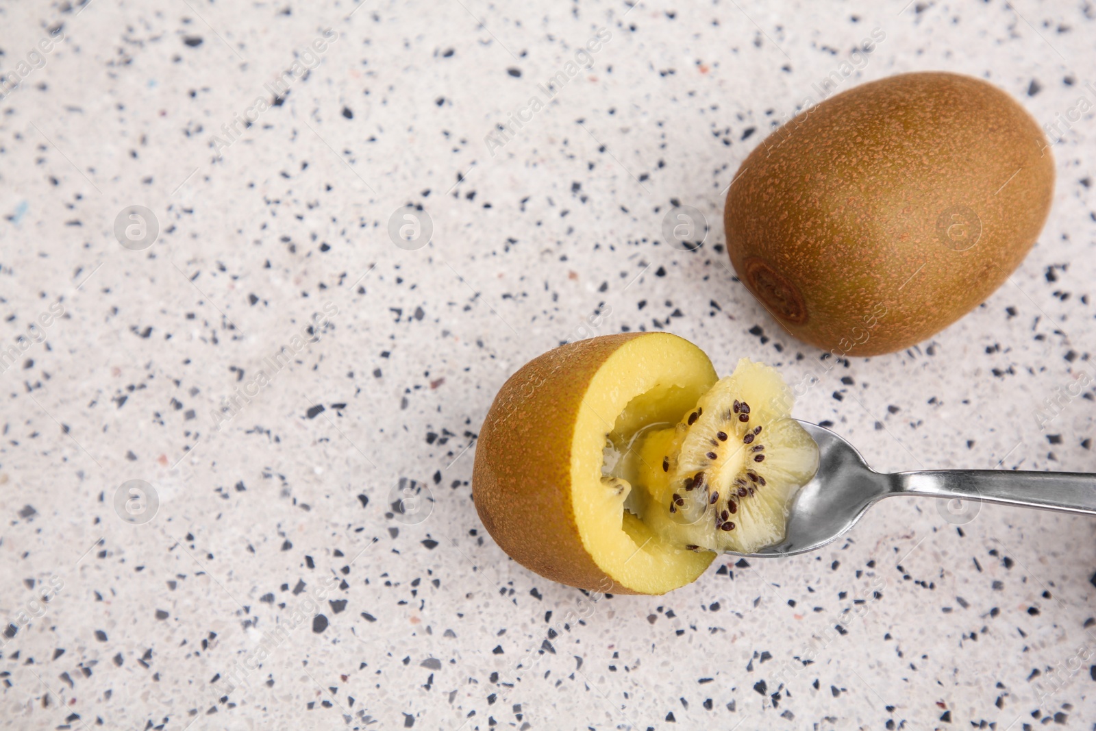 Photo of Spoon in fresh ripe yellow kiwi and fruits on white table with pattern, top view. Space for text