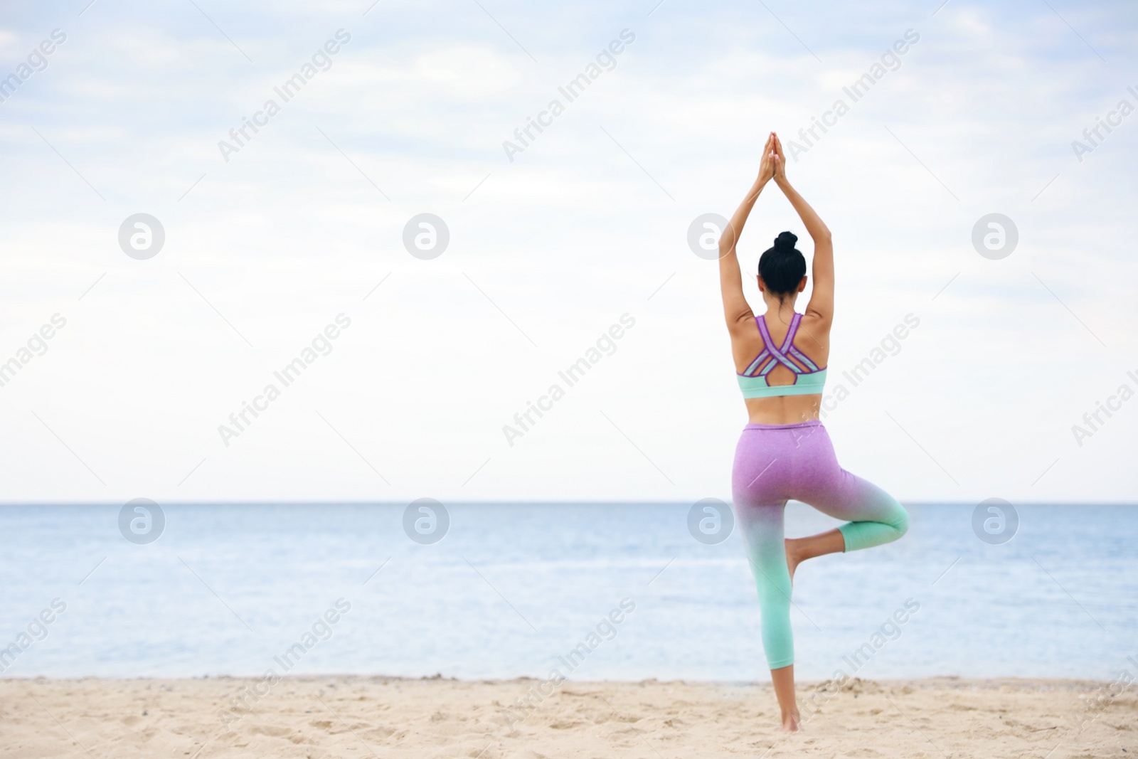 Photo of Young woman practicing yoga on beach, back view with space for text. Body training