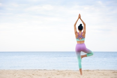 Young woman practicing yoga on beach, back view with space for text. Body training