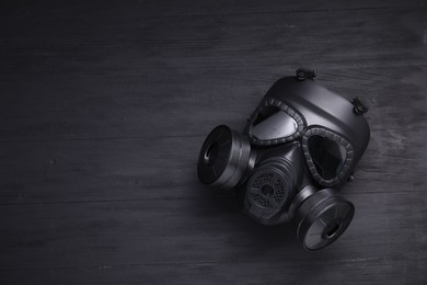 Photo of One gas mask on black wooden background, top view. Space for text