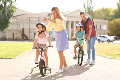 Photo of Happy parents teaching children to ride bicycles outdoors