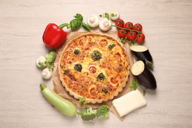 Delicious homemade vegetable quiche and ingredients on wooden table, flat lay