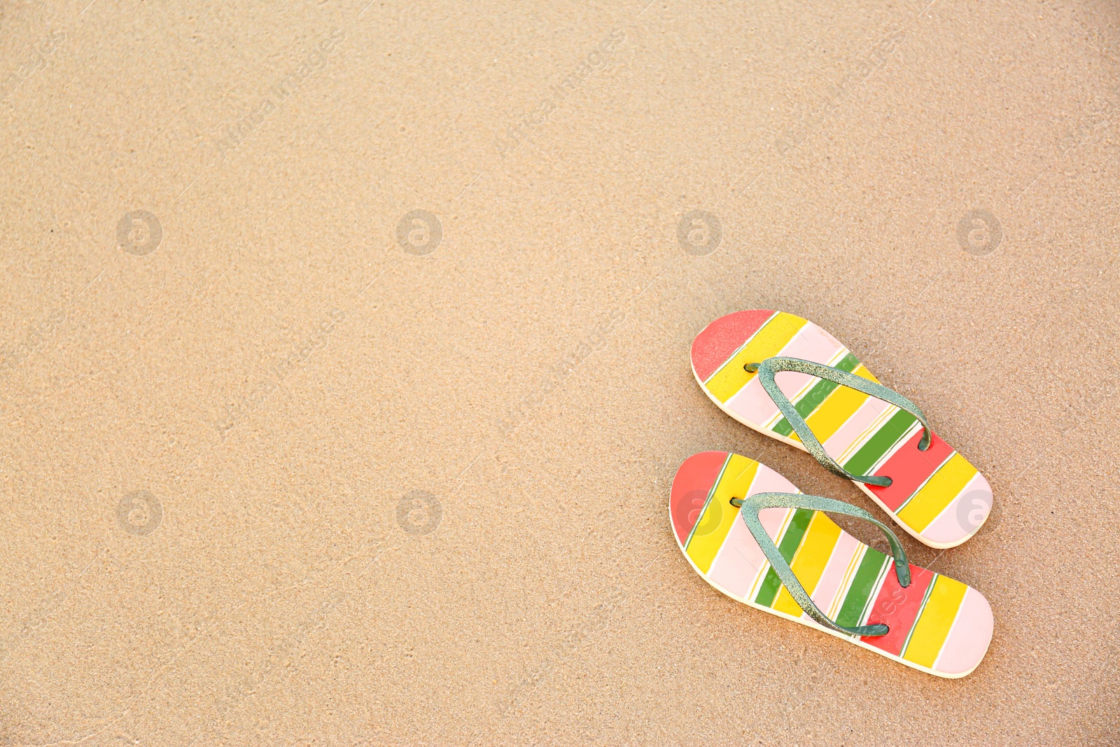 Photo of Stylish flip flops on sand, top view with space for text. Beach accessories