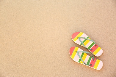 Photo of Stylish flip flops on sand, top view with space for text. Beach accessories