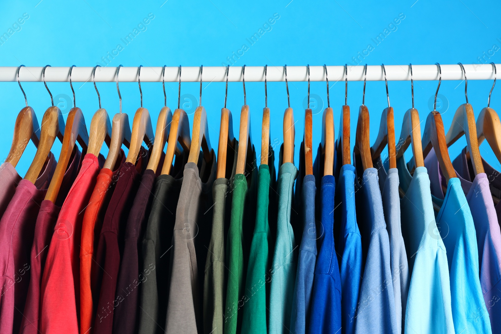 Photo of Colorful clothes on hangers against light blue background