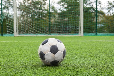 Dirty soccer ball on green football field against net