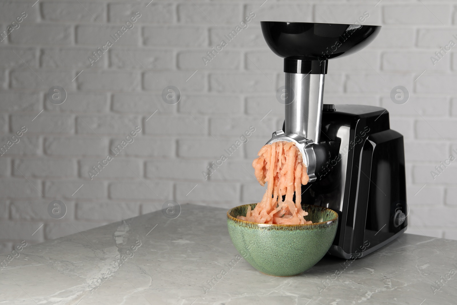 Photo of Electric meat grinder with chicken mince on grey marble table near white wall. Space for text