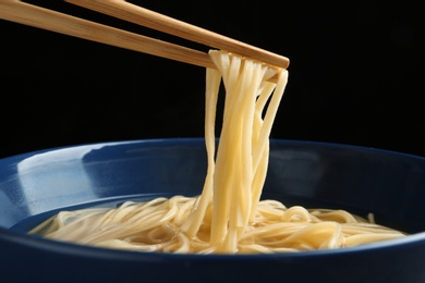 Eating noodle dish with chopsticks against black background, closeup