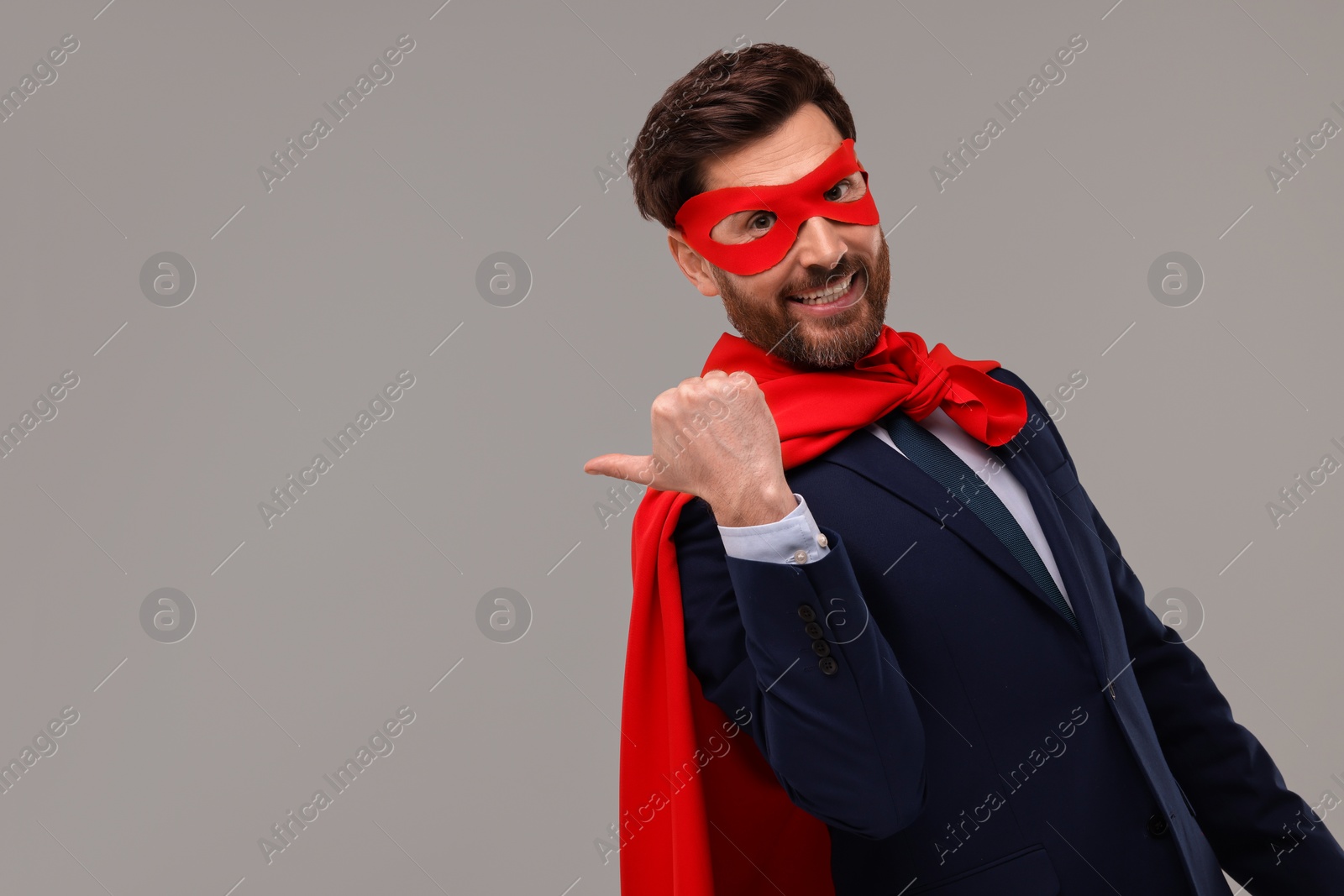 Photo of Happy businessman wearing red superhero cape and mask on beige background