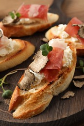 Photo of Delicious bruschettas with cheese, prosciutto and slices of black truffle on wooden table, closeup