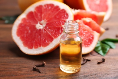 Bottle of essential oil and fresh grapefruit on wooden table