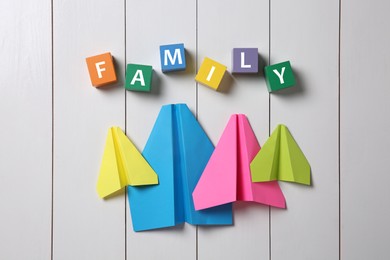 Paper planes and colorful cubes with word Family on white wooden background, flat lay