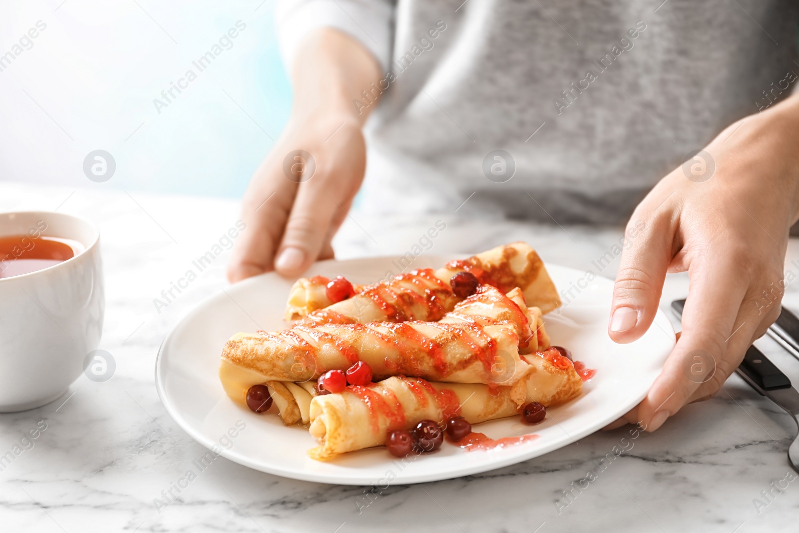 Photo of Woman putting plate with thin pancakes, berries and syrup on table