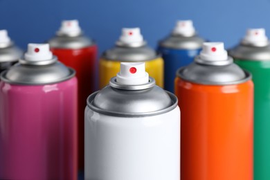 Photo of Colorful cans of spray paints on blue background, closeup