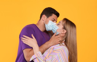 Couple in medical masks trying to kiss on yellow background