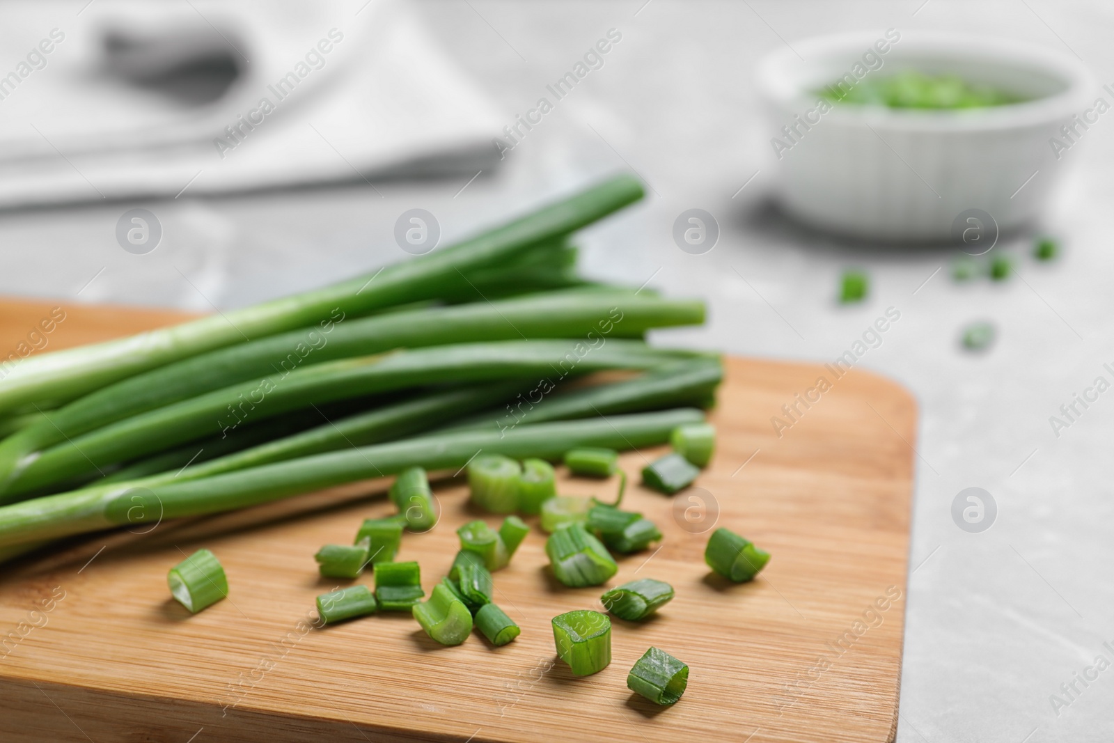 Photo of Wooden board with bunch of fresh green onion on table, closeup