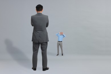 Small man shouting to giant boss on grey background