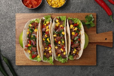 Delicious tacos with meat and vegetables on gray textured table, flat lay