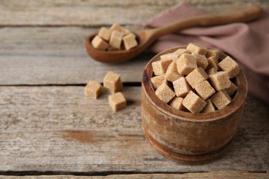 Photo of Bowl and spoon with brown sugar cubes on wooden table, closeup. Space for text