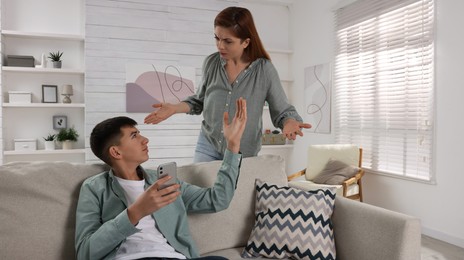 Photo of Mother scolding her son while he using smartphone at home. Teenager problems