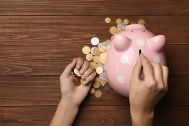 Woman putting coin into piggy bank on wooden background, top view
