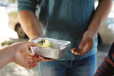 Photo of Poor man receiving food from volunteer outdoors, closeup