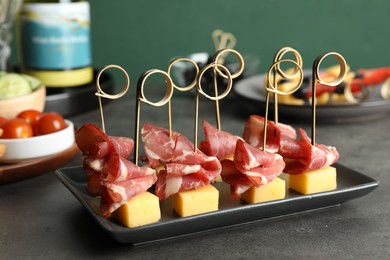 Photo of Tasty canapes with ham and cheese on grey table, closeup