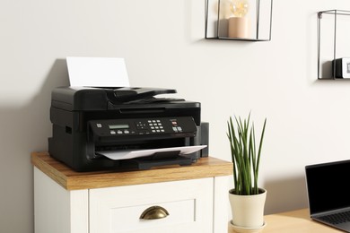 Photo of Modern printer with paper on chest of drawers indoors