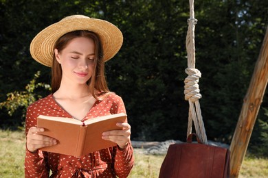 Beautiful young woman reading book outdoors on sunny day, space for text